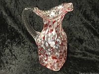 Photo of a hand blown glass pitcher, 7.5 inches tall, clear glass with red and white speckled design and clear twisted handle.
