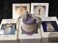 Photo of three boxed Hummel Christmas bells dated 1991, 1993, and 1994 along with two boxed Hummel collector plates dated 1985 and 1986.