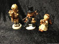 Front view of three Hummel porcelain figurines arranged side by side showing their distinct character features and paint detail.