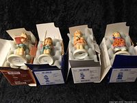 Photo of four assorted 3-inch Hummel porcelain figurines in original boxes with white foam padding inside and colorful box designs.
