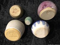 Photo showing bases of five pottery vases revealing artist signatures and markings.