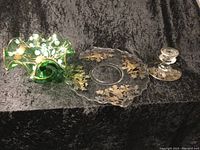 Photo showing three items: a green ruffled candy dish, a round silver etched glass plate, and a silver candle holder.