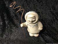 Front view of a 7-inch Inuit ceramic figurine holding a spiral shaped copper or brass wire on a black background.
