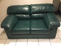 Front view of the first green leather love seat with plush arms and backrest.