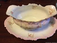 Gravy boat with attached underplate and floral design with gold trim on a wooden surface