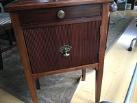 Front angle view of the vintage mahogany smokers cabinet showing drawer, tambour door, legs, and brass hardware.