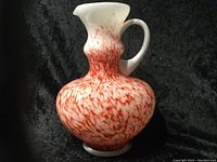 Side and angled view of the milk glass pitcher showing red speckled design on the exterior and bulbous shape.