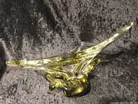 Image of an elongated, curved Murano glass ashtray with yellow accents on a dark cloth background.