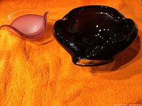 Two Murano glass items on an orange background: a deep purple ash tray and a pink and clear dish.