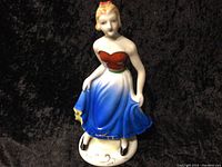 Front view of the porcelain figurine of a woman in a colorful dress set against a black background.