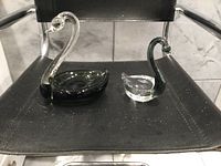 Photo showing both Venetian glass swans on a black chair seat, highlighting their size and contrasting colors.