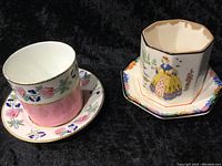 Two jam pots with matching saucers, displaying different floral and figurative decorations, on a black background.