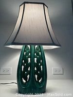 Front view of ceramic table lamp illuminated, showing the cream fabric shade and emerald green ceramic base with grape and leaf cutout design.