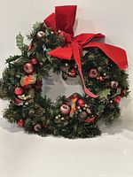 Full view of vintage artificial Christmas wreath showing evergreen foliage, red tinsel, artificial apples, pine cones, ribbons and large red felt bow.