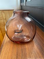 Side view of Jean Vallières hand-blown glass decanter/vase with soft amethyst amber hue, sitting on wooden surface beneath window light.