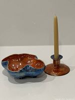 Photo showing side view of ceramic bowl with scalloped rim and candle holder with candle inserted, highlighting blue and orange/rust finishes