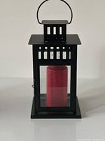 Front view of black metal lantern with glass sides and red candle inside.