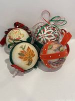 Four handmade Christmas ornaments made from Styrofoam balls with fabric and ribbon decoration including Santa Claus, autumn leaves, floral pattern, and quilting design detail.