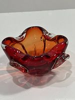 Amber red MCM art glass ashtray showing wavy, thick glass shape from an overhead front angle.