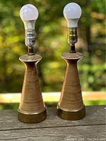 Front view of the pair of ceramic lamps showing the beige bodies with a gold wash and brass bases. Both lamps have light bulbs installed.