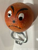 Front close-up of the teak handle with the hand-painted grumpy face and metal bottle opener base.