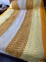 Close view of the blanket showing the lacey chevron crochet pattern and warm yellow, beige, and mustard colors.