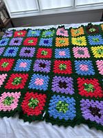 Photo showing colorful granny square crochet pattern on the blanket with a dark green border, laid out flat near window light.