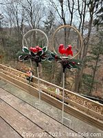 Full view of both outdoor cardinal garden stakes on a wooden deck, showing the metal frame and ground push feet