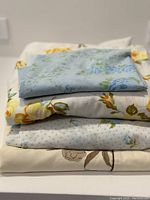 Stacked view of four folded vintage bedding pieces showing various floral patterns including blue, yellow, and brown roses and florals.