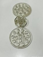 Three clear glass flower frogs arranged vertically showing two larger 5 inch diameter frogs and one smaller 3 inch diameter frog in the middle.