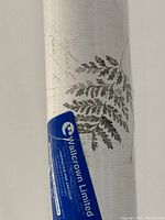 Partial view of the rolled wallcovering with a blue Wallcrown Limited label showing brand and manufacturing origin (Canada). Leaf pattern visible on textured vinyl surface.