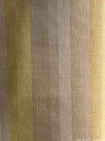 Close-up photo of vintage vinyl wallpaper roll showing wide stripes in soft yellow, gold, taupe, and white with a coated vinyl texture and subtle grid weave.