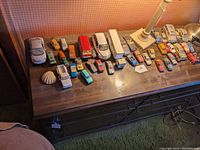 Top view of a dresser with approximately 30 dusty toy cars and vehicles arranged on top, along with an ornamental shell-shaped object.