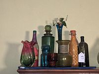 Front view showing the collection of colorful glass vases, bottles, jars with various designs and styles, placed on top of a wooden hutch.