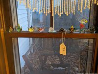 Wide view of nine small decorative glass items on wooden window ledge, mostly Lenox teapots and figurines