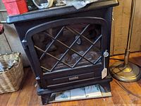 Front view of the black Duraflame electric heater stove showing the glass door with metal grille and the interior faux logs.