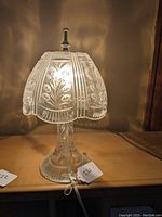 Lamp illuminated on wooden surface showcasing etched floral and leaf patterns on shade and base.