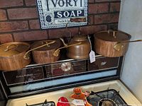Four copper cookware pieces displayed on a stove: three saucepans with lids and a tea kettle