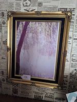 Frontal photo of gilt picture frame with landscape photo depicting trees and mist