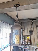 Full view of the gray metal lantern hanging from a bale hook attached to a wooden ceiling beam, electric candle visible inside.