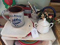 Photo showing Melrose stoneware mug on top of kitchen trivets, the white sugar bowl beside it with lid and handles. A red vintage radio and flower basket behind.