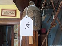 Side view of the rustic primitive cowbell showing the wooden handle and attached number tag.