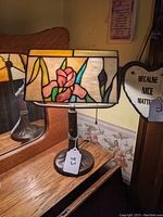 Full view of Tiffany style bankers desk lamp on wooden surface with stained glass floral shade and pull chain.