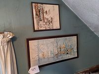 Photo showing both framed mounted prints on a wall under a staircase, one above the other.