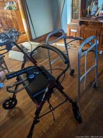 Photo showing both mobility devices; the rolling walker with seat and the folding walker in a room with wooden floor and furniture.