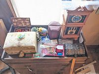 Overview of six jewelry boxes on wooden bench with fabric embroidered box, wooden sticker-lid box, burgundy hex box, metal chest and clock-shape box alongside a red divided tray of jewelry