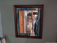 Full view of the rectangular oak framed stained glass mirror hung on a gray wall.