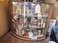 Front view of the Hughes Brushes cabinet showing curved glass front and multiple small figurines inside on three glass shelves.