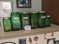 Photo showing all six green ribbed glass canisters arranged in a row with some missing lids and labels.