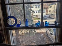 Window ledge with blue glass ornamental items including circular sun catcher, whale figurine, and glass bottle seen in natural light